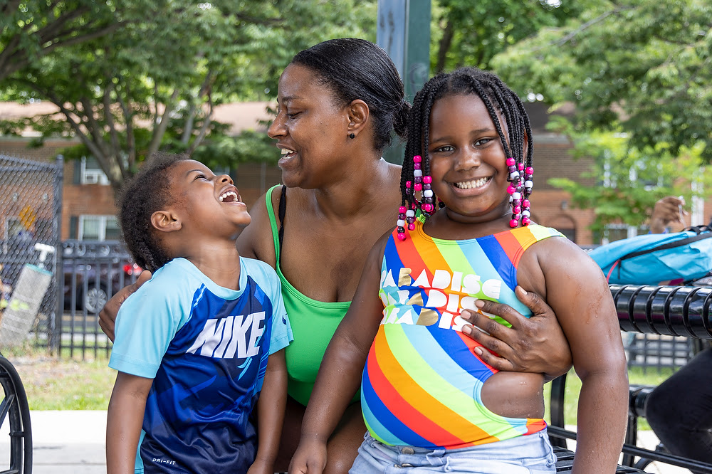 A Black mother holding her son and daughter, smiling and laughing.